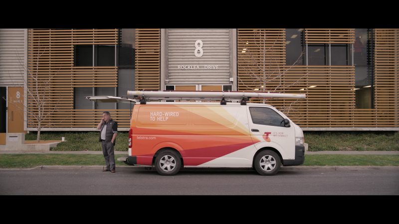 Telstra van parked with man standing at rear talking on phone outside building