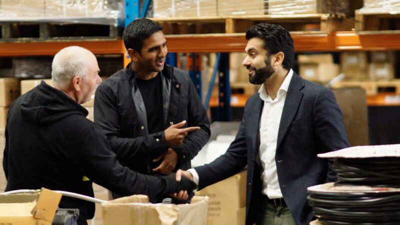 Three men in warehouse smiling and shaking hands