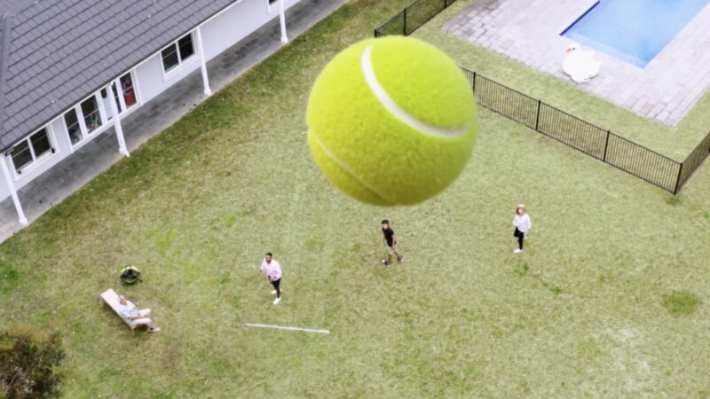 Tennis ball in air above backyard cricket game