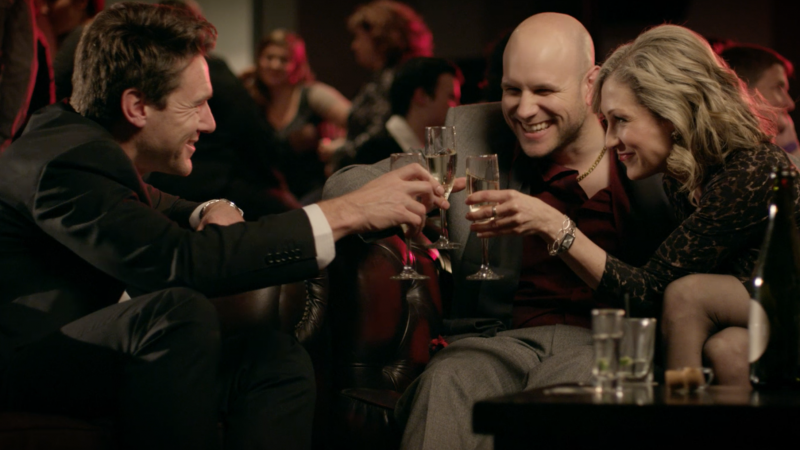 Two men and woman smiling and saluting with drinks in bar