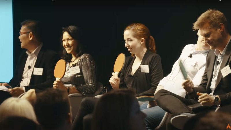 5 people sitting on stage smiling and holding table tennis bats up