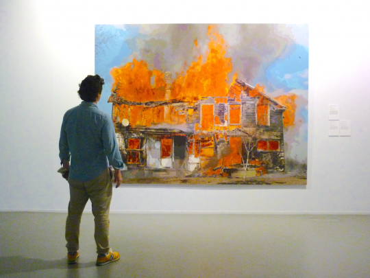 Man looking at painting of burning house in gallery